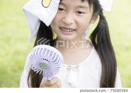 Elementary school girl who sweats and cools with a handy fan Elementary school girl who sweats and cools with a handy fan 75080364