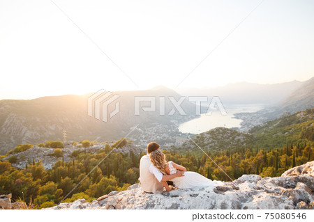 The bride and groom are embracing on Mount Lovcen, a picturesque panoramic view of the Bay of Kotor opens in front of them The bride and groom are embracing on Mount Lovcen, a picturesque panoramic view of the Bay of Kotor opens in front of them 75080546