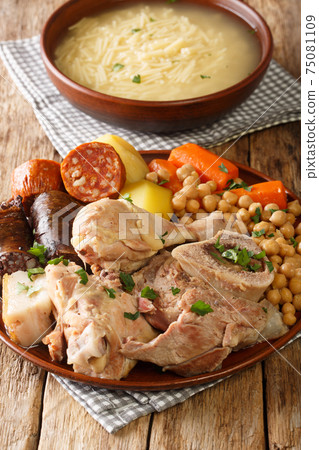 Madrid cocido meat, potato and chickpea stew close-up on a plate. Vertical 75081109