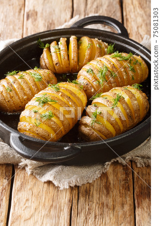 Delicious hasselback potatoes baked with butter, herbs and garlic close-up in a pan. Vertical 75081303