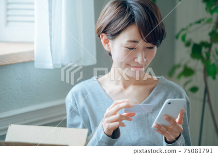 A middle-aged housewife who makes card payments while checking the internet on her smartphone 75081791