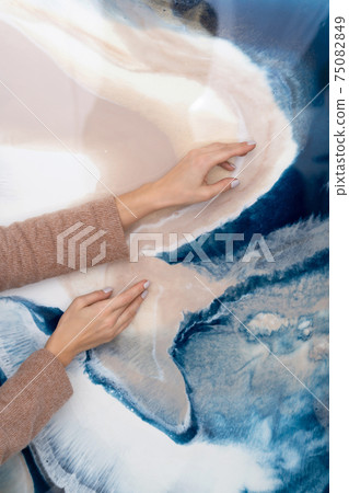 Hands of a young woman against the background of a painting in fluid art technique, resin art. 75082849
