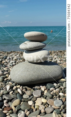 Four round stones lie in a pyramid on the shore of the blue sea 75084342