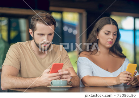 Man and woman staring intently into smartphones in cafe 75086180