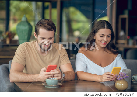 Man and woman with smartphones in cafe Man and woman with smartphones in cafe 75086187