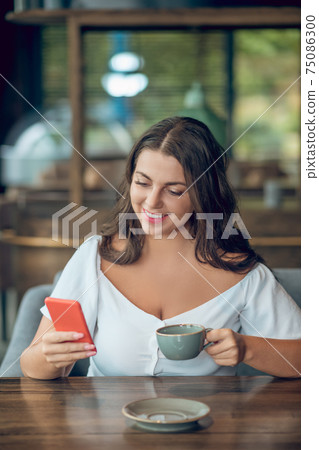 Involved joyful woman looking into smartphone in cafe 75086300