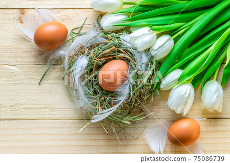 Easter colourful eggs in basket with spring tulips, white feathers on wooden table background in Happy Easter decoration. Spring holiday flat lay concept. 75086739