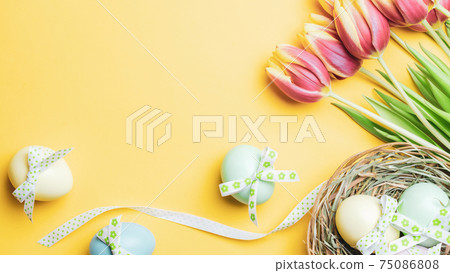 Easter eggs Colourful egg with tape ribbon, spring tulips, white feathers on pastel yellow background in Happy Easter decoration. Festive decoration in flat lay. 75086808