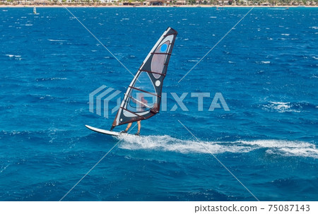 the windsurfer on the board under sail moves at a speed along the surface of the sea the windsurfer on the board under sail moves at a speed along the surface of the sea 75087143