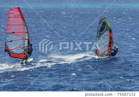 two windsurfers on sailboards are moving at a speed along the sea surface 75087152