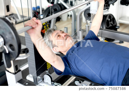 A gray-haired senior man doing a bench press at the gym 75087386