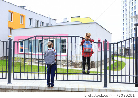 Children with briefcases over their shoulders on the background of the school. 75089291