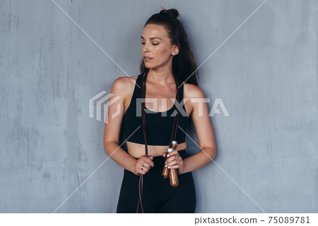 Portrait of a sporty girl with a skipping rope standing against the wall 75089781