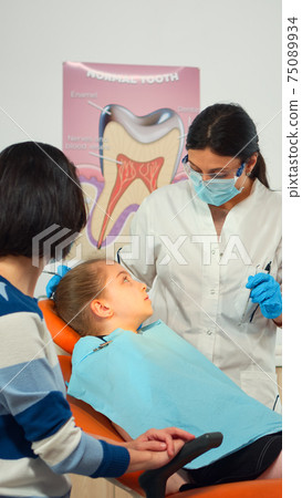 Pediatric nurse and dentist doctor working in modern dental clinic treating little girl 75089934