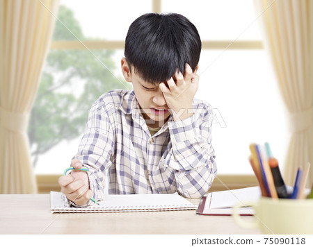 10 year-old asian elementary schoolboy appears to be frustrated while doing homework at home 75090118