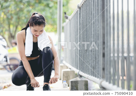 Runner woman getting ready to run tying running shoes laces. Healthy lifestyle jogging motivation closeup of feet or footwear. 75090410