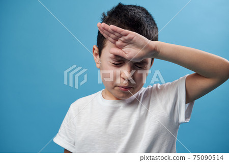 Boy holding his temple. Facial emotion on blue background with copy space. Closeup 75090514