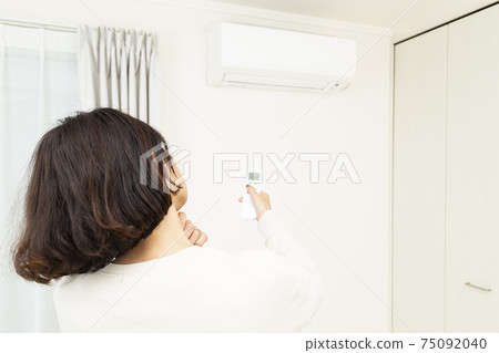 A woman who operates the remote control of the air conditioner A woman who operates the remote control of the air conditioner 75092040