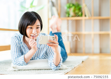 一個年輕的女人,看著她的智能手機上的視頻 一個年輕的女人,看著她的智能手機上的視頻 75092155