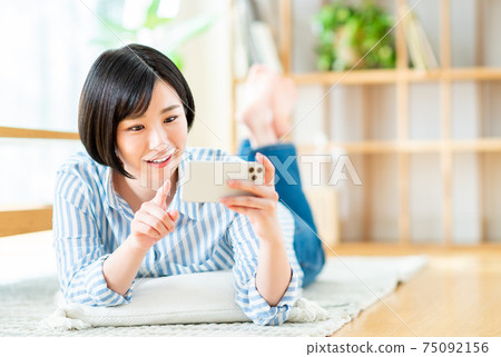 一個年輕的女人，看著她的智能手機上的視頻 75092156