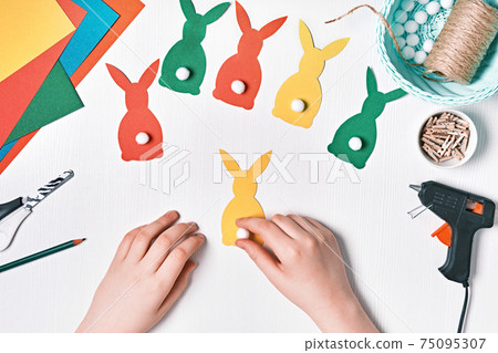 DIY Easter home decor from natural materials. Hands make garland of colored paper, twine and pom-poms DIY Easter home decor from natural materials. Hands make garland of colored paper, twine and pom-poms 75095307