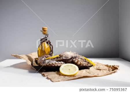 Seafood, whole raw big octopus on a plate with lemons and olive oil ready for preparing Seafood, whole raw big octopus on a plate with lemons and olive oil ready for preparing 75095367