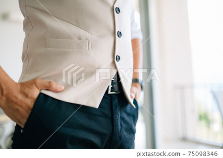 A man holding his hands in his pants pockets in a hotel room while preparing for a wedding ceremony  75098346