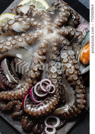 Seafood, whole raw big octopus on a stone dish served with mussels, lemon and red onion Seafood, whole raw big octopus on a stone dish served with mussels, lemon and red onion 75098964