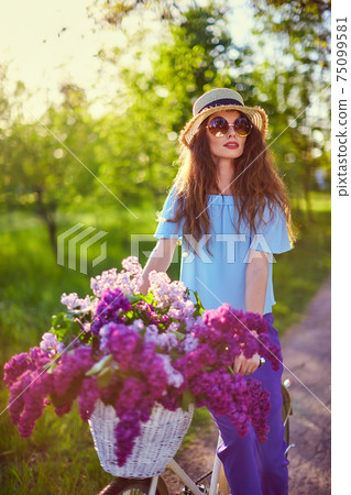 Portrait of a happy beautiful woman in straw hat with vintage bicycle and flowers on park background in the sunlight outdoor. Portrait of a happy beautiful woman in straw hat with vintage bicycle and flowers on park background in the sunlight outdoor. 75099581
