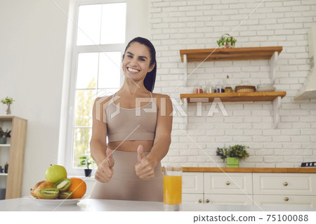Happy slender female athlete raises thumbs up showing that fresh fruit juice and fruit is super. Happy slender female athlete raises thumbs up showing that fresh fruit juice and fruit is super. 75100088