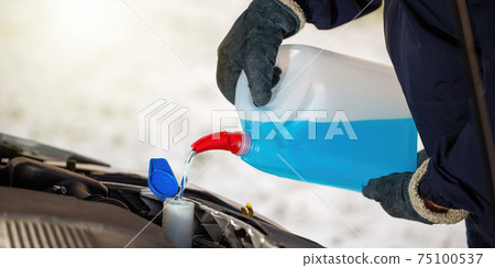 Man with gloves pouring antifreeze coolant into car reservoir in winter season. 75100537