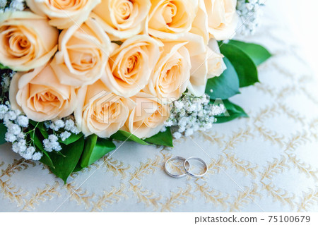 Beautiful wedding rings lie on light surface against background of bouquet of flowers. Declaration of love, spring. Wedding card, Valentine's Day greeting. Wedding rings. Wedding day details. Beautiful wedding rings lie on light surface against background of bouquet of flowers. Declaration of love, spring. Wedding card, Valentine's Day greeting. Wedding rings. Wedding day details. 75100679