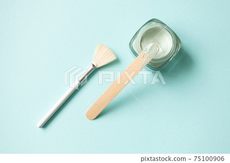 Facial green clay mask in glass jar, wooden stick and make-up brush on light blue background Facial green clay mask in glass jar, wooden stick and make-up brush on light blue background 75100906