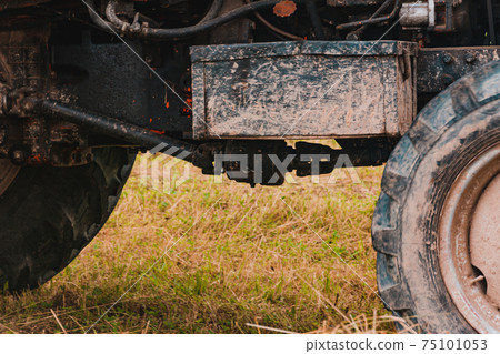 Old red tractor in the field during the haymaking season, pressing hay on bales, forage harvesting. 75101053