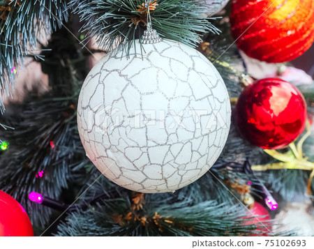White Christmas ball hanging on a pine branch with in the center of the frame among other decorations White Christmas ball hanging on a pine branch with in the center of the frame among other decorations 75102693
