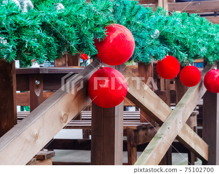 Red glossy and matte christmas balls hang on green spruce branch on wooden railing Red glossy and matte christmas balls hang on green spruce branch on wooden railing 75102700
