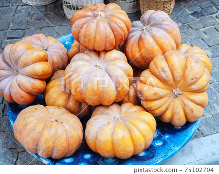 A blue ceramic bowl with orange pumpkins stands on rough paving slabs outside A blue ceramic bowl with orange pumpkins stands on rough paving slabs outside 75102704