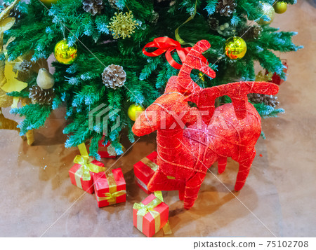 Red figurine of a deer and boxes with gifts stand under the christmas tree Red figurine of a deer and boxes with gifts stand under the christmas tree 75102708