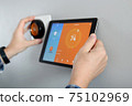 Man is Adjusting a  temperature using a tablet with a smart home app in modern living room 75102969
