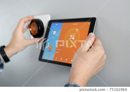 Man is Adjusting a temperature using a tablet with a smart home app in modern living room Man is Adjusting a temperature using a tablet with a smart home app in modern living room 75102969