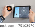 Man is Adjusting a  temperature using a tablet with a smart home app in modern living room 75102970