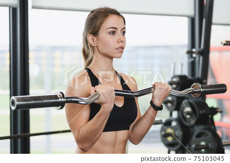 Cute girl has a hard athletic workout in the gym, doing exercises with barbells. Cute girl has a hard athletic workout in the gym, doing exercises with barbells. 75103045