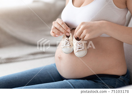 Closeup Shot Of Pregnant Woman Holding Small Baby Shoes Near Her Belly Closeup Shot Of Pregnant Woman Holding Small Baby Shoes Near Her Belly 75103178