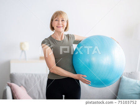 Portrait of joyful senior woman holding fitness ball and smiling at camera, indoors Portrait of joyful senior woman holding fitness ball and smiling at camera, indoors 75103752