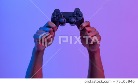 Black male hands holding joystick for video games over purple neon background Black male hands holding joystick for video games over purple neon background 75103946