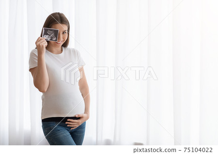 Happy Pregnant Woman With Ultrasound Scan Image Posing Near Window At Home Happy Pregnant Woman With Ultrasound Scan Image Posing Near Window At Home 75104022