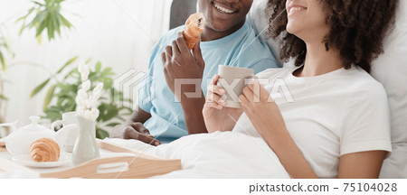 Young beautiful loving african american couple sits in bed, man and woman holds cups and drinks hot tea Young beautiful loving african american couple sits in bed, man and woman holds cups and drinks hot tea 75104028