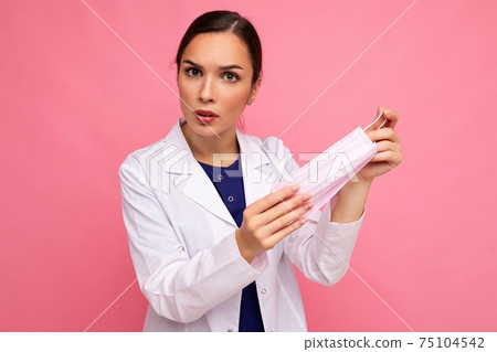 Portrait of an angry attractive young female doctor in white coat holding medical mask standing Portrait of an angry attractive young female doctor in white coat holding medical mask standing 75104542