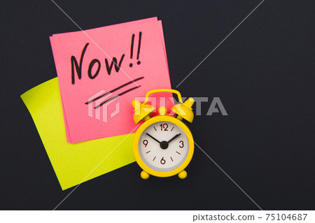 Sticker with handwriting the word NOW on alarm clock on dark blue background with copy space using as stop procrastination, self discipline or motivation to complete task Sticker with handwriting the word NOW on alarm clock on dark blue background with copy space using as stop procrastination, self discipline or motivation to complete task 75104687