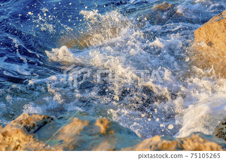 Waves crushing on the rocks on beach in the morning time. Sunrise on the wavy sea with rocks.  75105265
